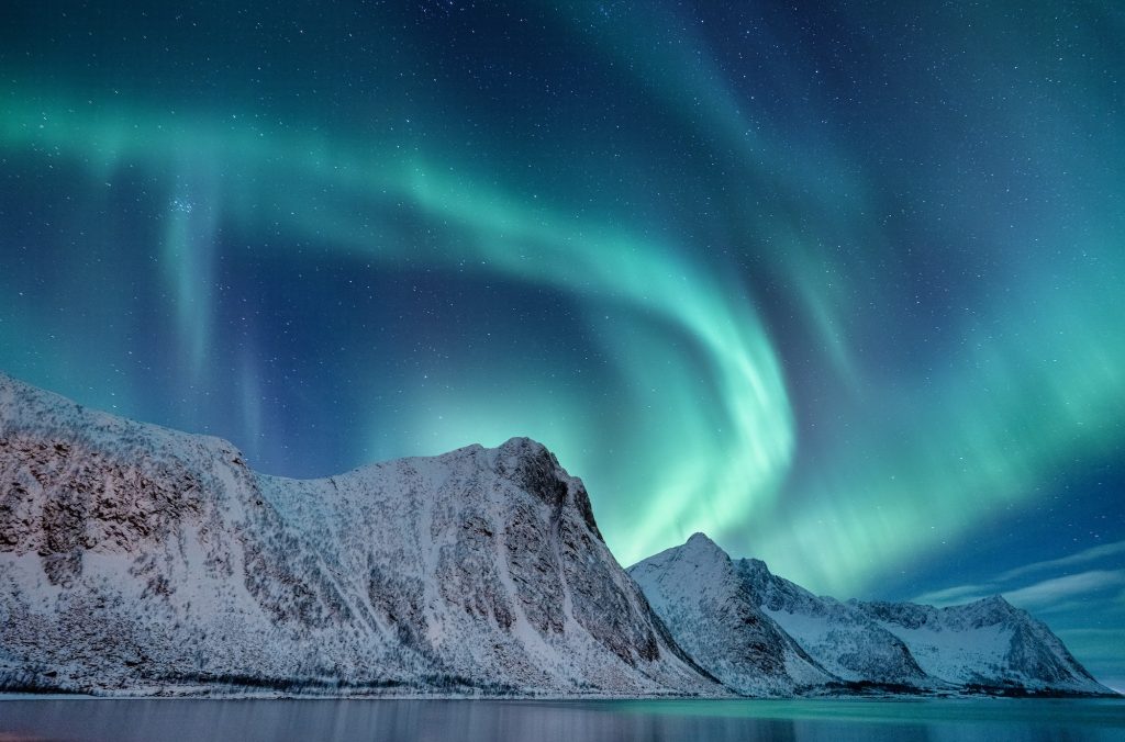 Aurora borealis in Norway. Green northern lights above mountains. Night winter landscape with aurora