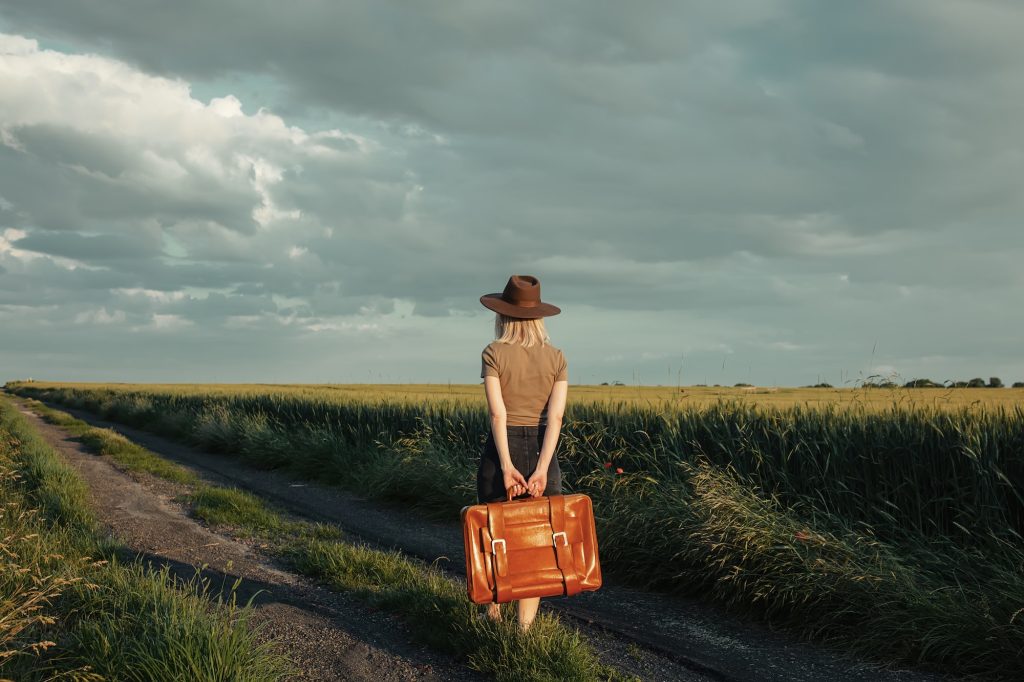 Beautiful blonde girl with suitcase in countryside road in sunset time