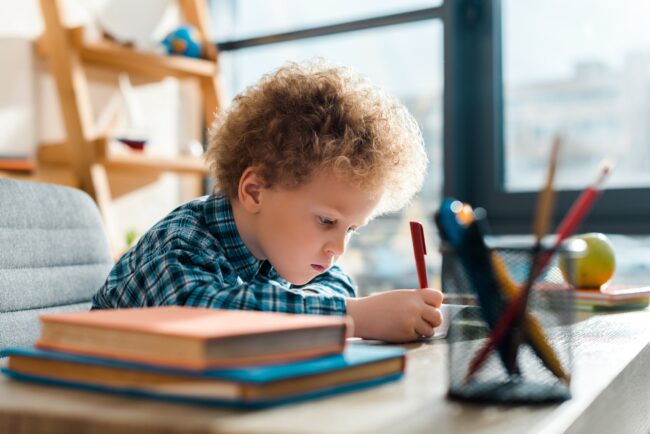 selective focus of curly kid writing near books