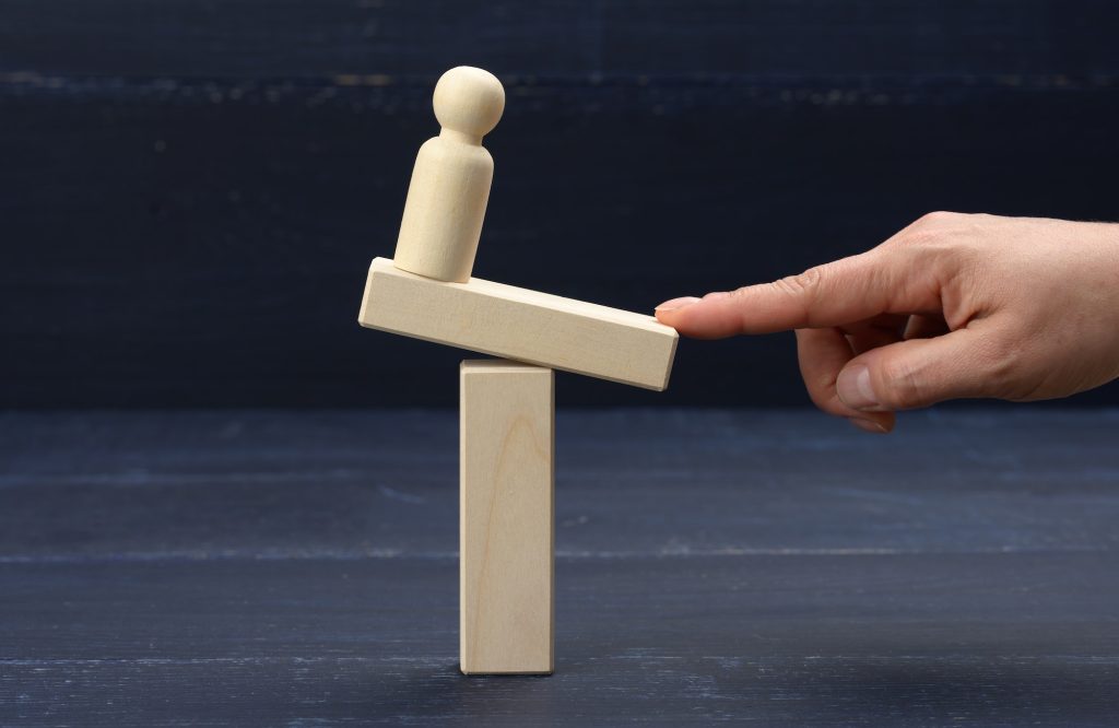 Wooden figure of a man stands on a swing, his finger keeps balance. Concept of help